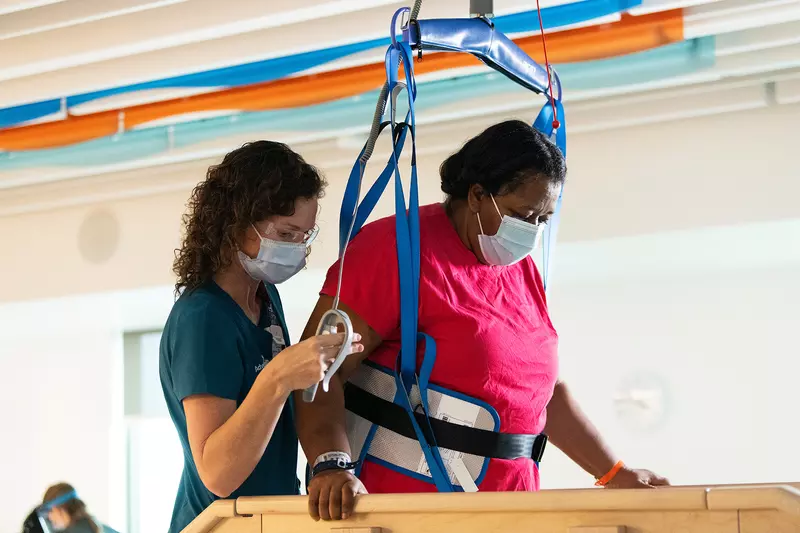 Physical therapist helping a patient in rehab with a walking exercise with the patient is being supported by a harness.