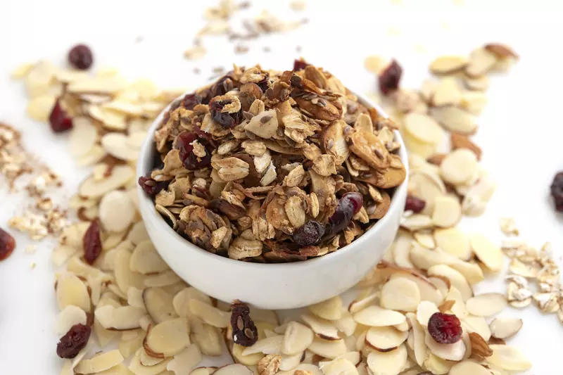 White bowl of granola surrounded by sliced almonds