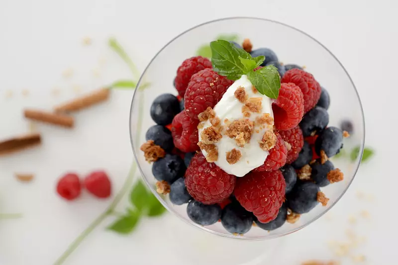 a clear glass bowl filled with creamy yogurt and a mix of berries, granola and topped with mint leaves