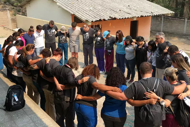 A group of doctors, employees, and volunteers in a circle of prayer