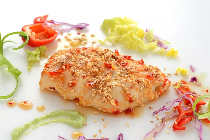 a serving of prepared chicken, coated in sesame seeds and surrounded by shredded cabbage