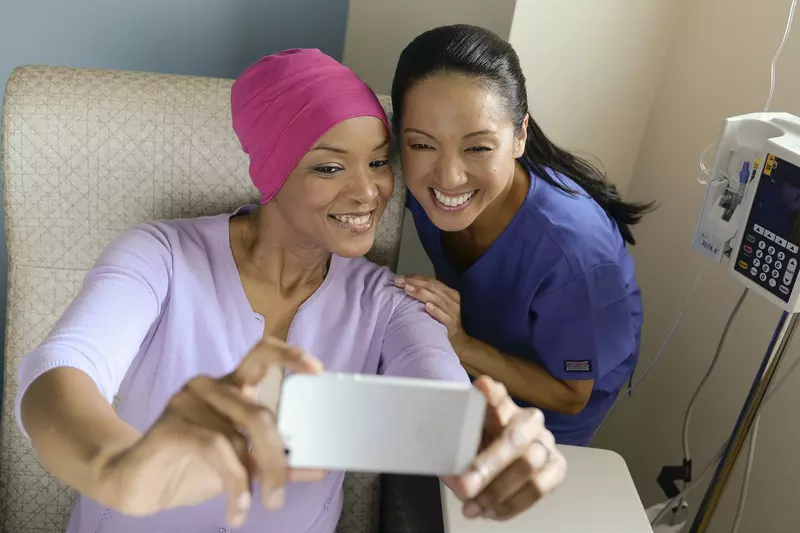 A female African American cancer patient takes a selfie with a female Asian nurse.