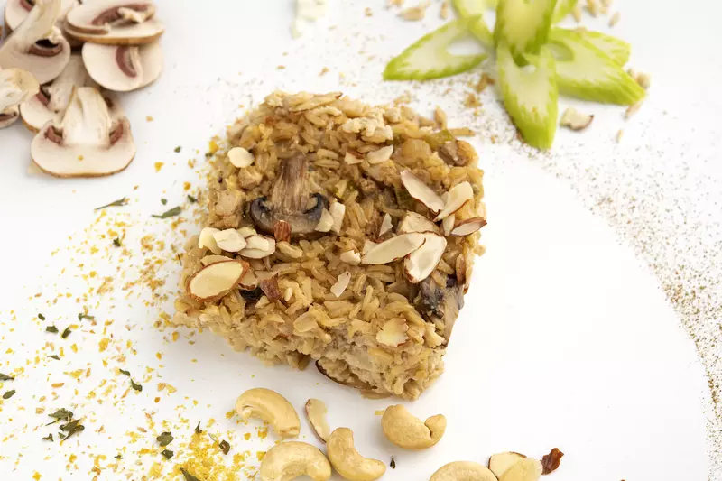 Square of almond chick'n rice on white surface with mushroom decoration