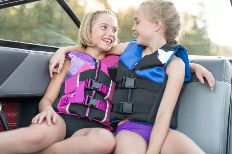Two little girls, arms around each other, sitting on a boat, wearing life vests.