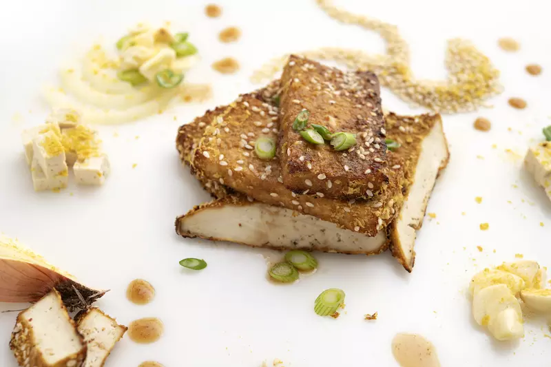 three tofu steaks on white surface with nutritional yeast garnish