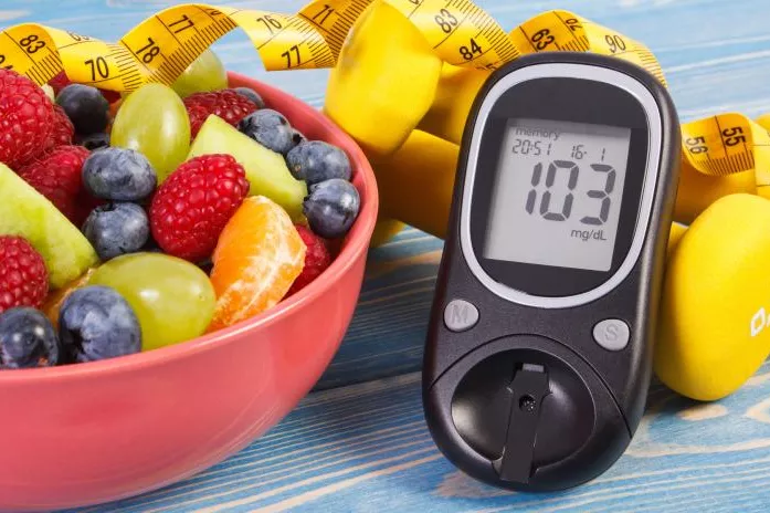 A Bowl of Fruit and a Glucose Checker Lay on a Countertop 