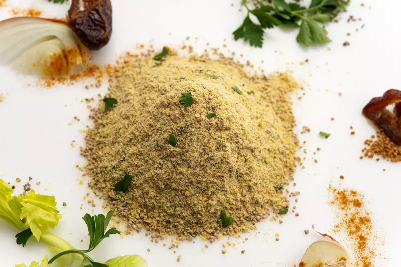 Mound of chicken-style seasoning on white surface surrounded by garnishes