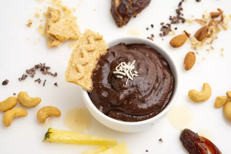 Carob pudding in bowl with a pie crust garnish, surrounded by decorative nuts