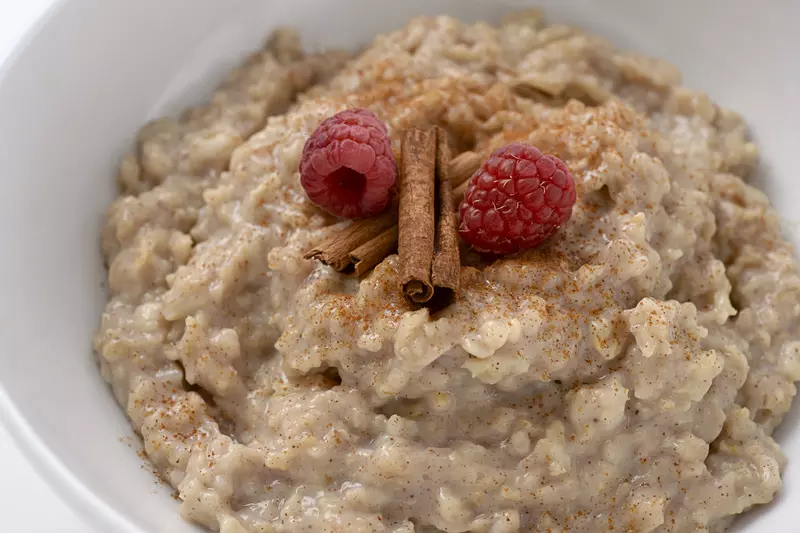 a bowl filled with a sweet cinnamon oatmeal mixture, topped with two raspberries and a cinnamon stick