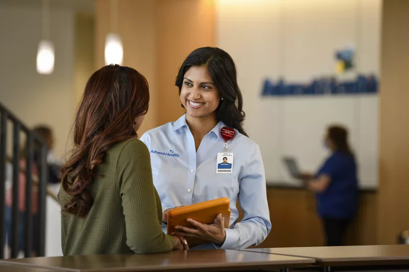 A smiling AdventHealth Employee welcomes a patient at the front desk.