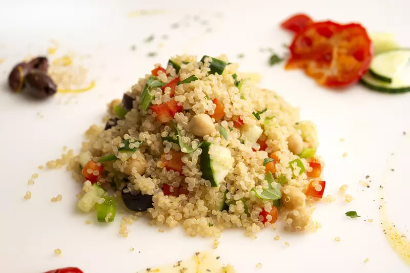 Mound of quinoa on white surface with red bell pepper garnish