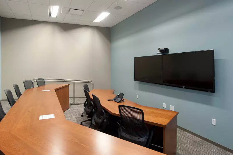 A meeting room where a wide screen tv, with a webcam, is pointing at two vertical-aligned tables.