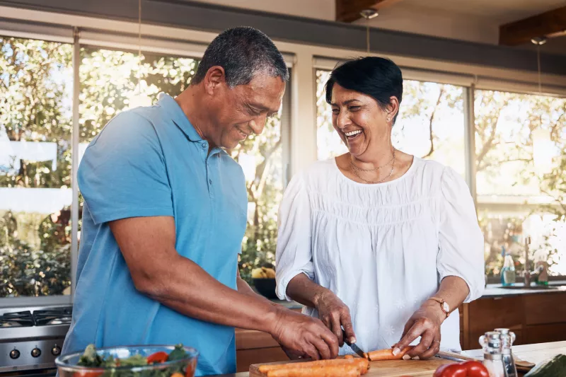 A couple cutting up carrots for a salad while in a kitchen.