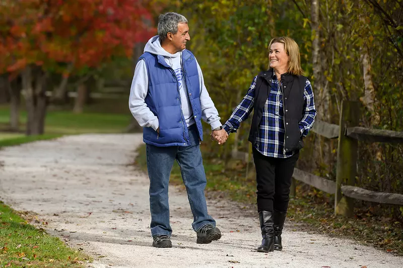 Couple walking down a path outdoors in the fall holding hands.