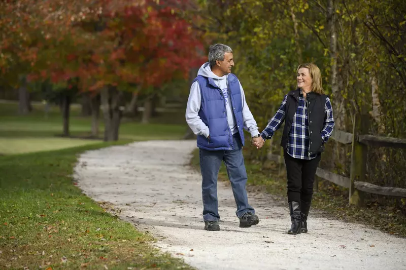 Couple walking down a path outdoors in the fall holding hands.