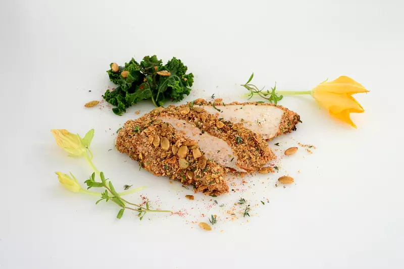 a serving of chicken, coated in a pumpkin seed crisp, sliced into three pieces