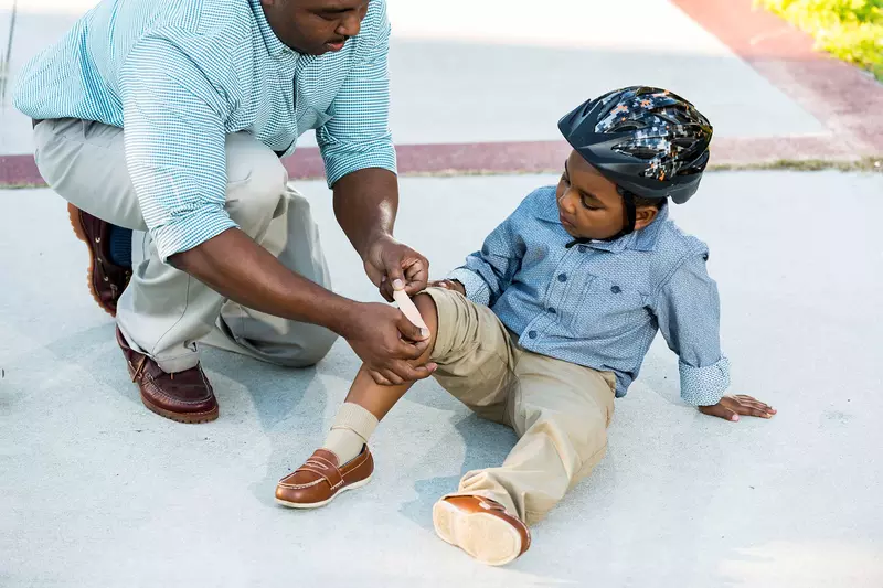 A father puts a bandage on his son's knee. 