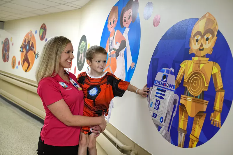 Boy patient with AdventHealth for Children employee looking at a wall with C-3PO and R2-D2
