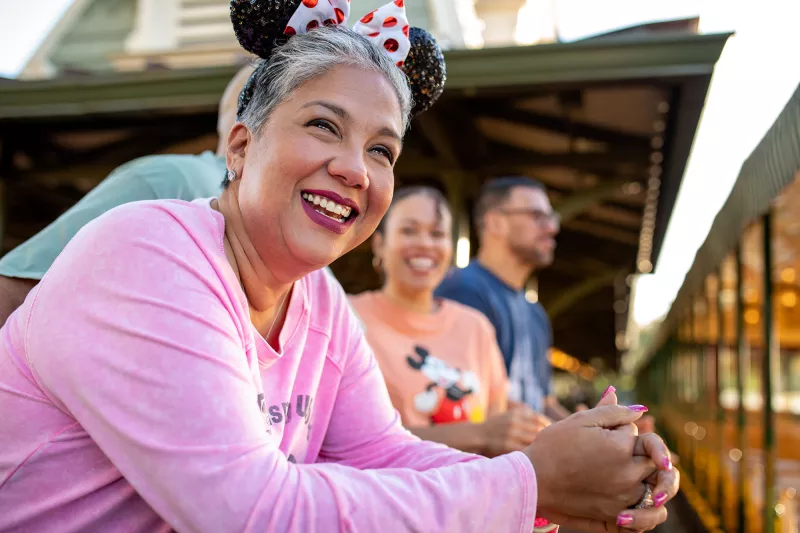 A senior woman smiling and wearing a Minnie Mouse headband in the foreground with her family in the background at Walt Disney World® Resort.