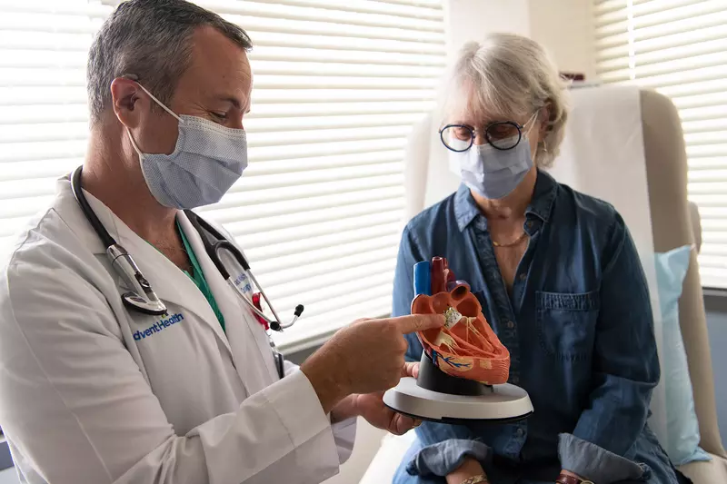Doctor showing a woman patient a heart model while both wear masks.