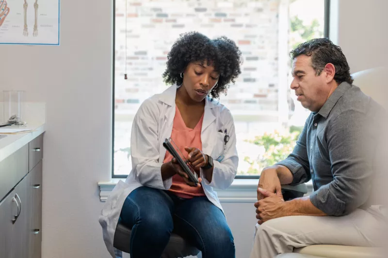 A female doctor showing a male patient test results in a examination room.