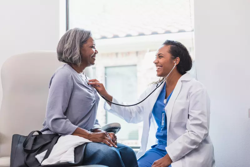 Doctor listening to an older woman patient's heart.