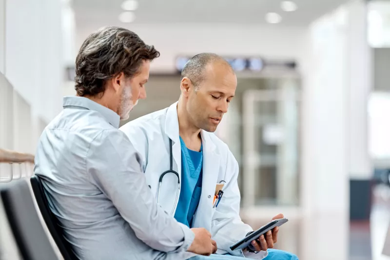 A physician and his male patient read documents together.
