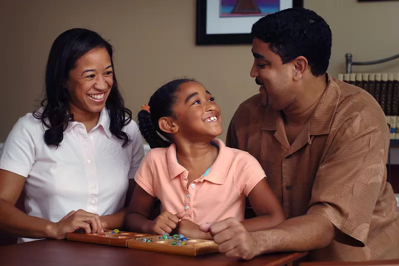 A daughter smiles at her father while playing a game with her parents. 