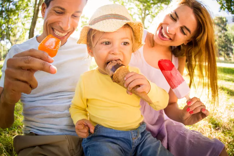 Family of three, sitting on the ground eating popsicles