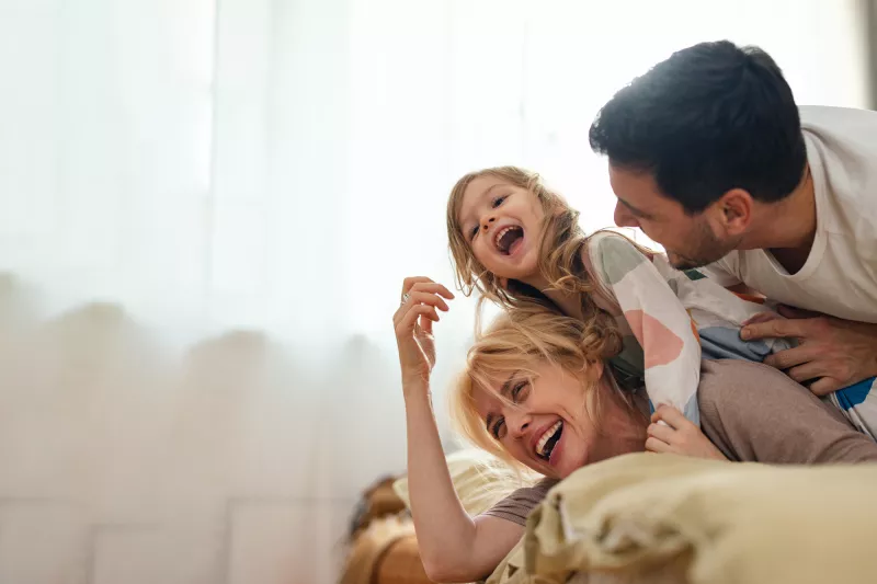 A family laughing while laying on a bed at home.