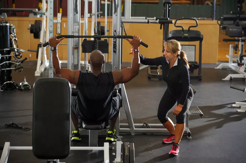 Female personal trainer coaching male trainee with a lat pulldown exercise.