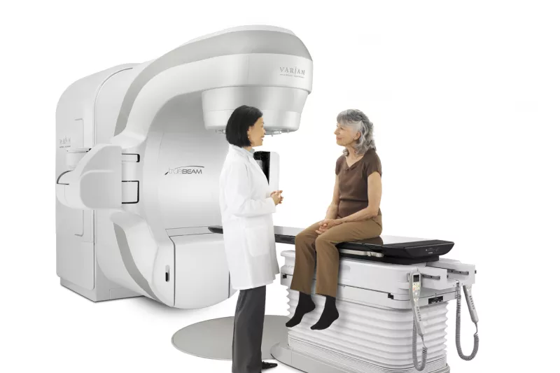 Oncologist with a female patient sitting on the bed of the TrueBeam Radiotherapy System from Varian Medical Systems.