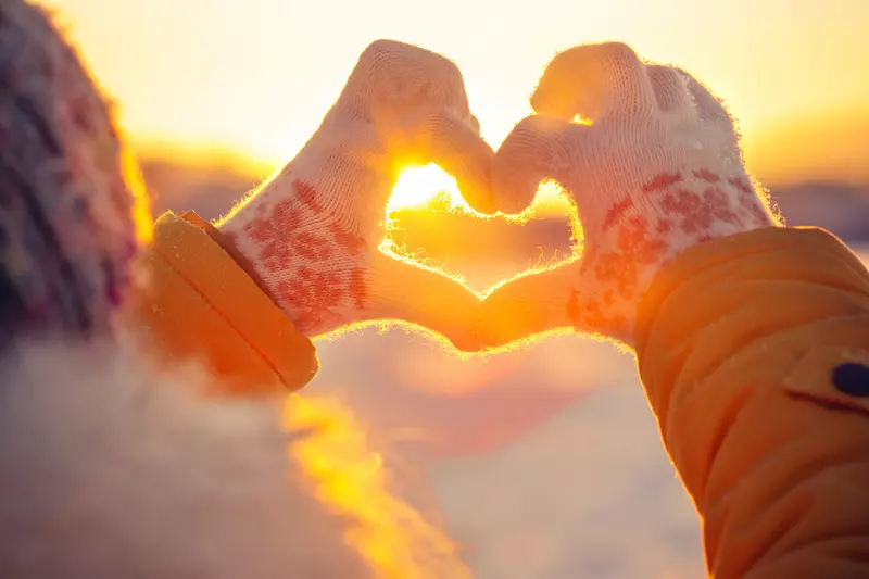 Woman in winter clothing making a heart with her hands.