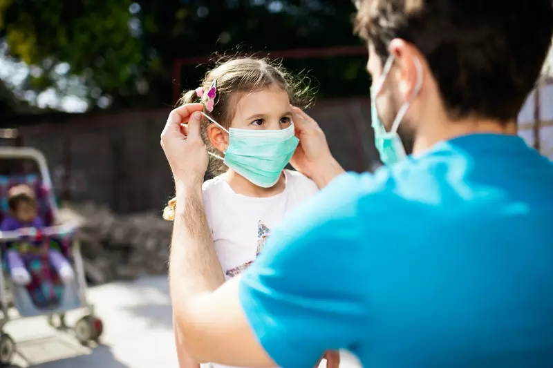 A father putting a mask on his daughter before going out