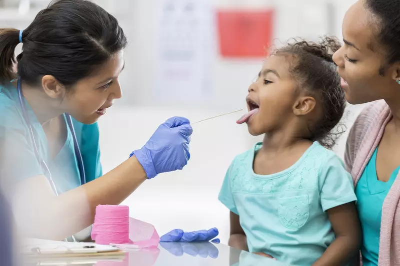 Little girl sitting on her mother's lap sticking her tongue out for the doctor.