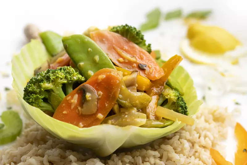 Lettuce bowl filled with veggie stir-fry sitting on brown rice