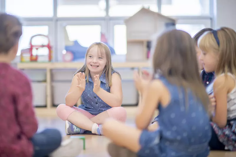 A cute little girl with Down syndrome smiles as she claps along to music with her friends.