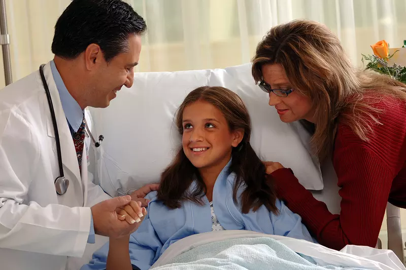 A young patient with her mom holds the hand of her doctor.