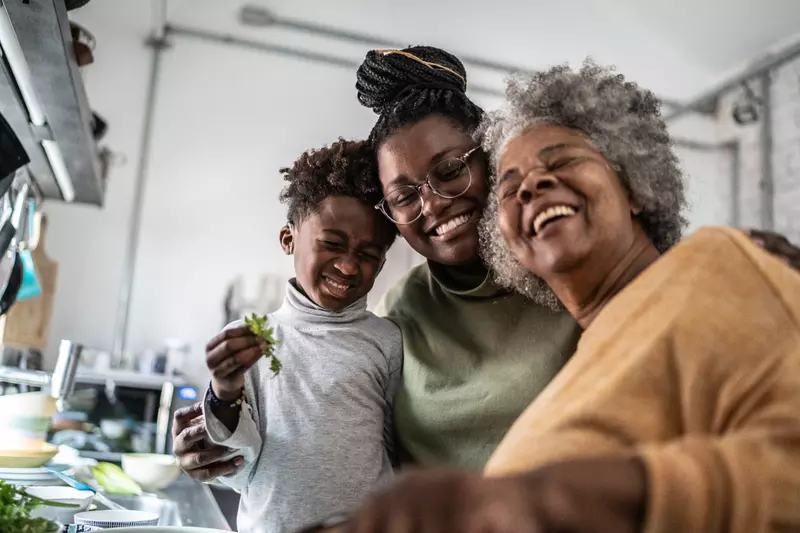 Grandmother, mother, and son smiling together while in the kitchen at home.
