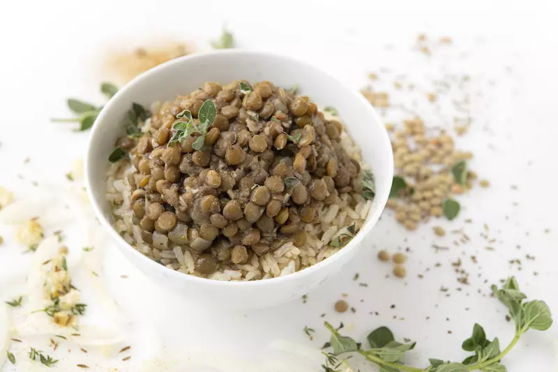 Bowl of lentils and rice on white surface with green garnish