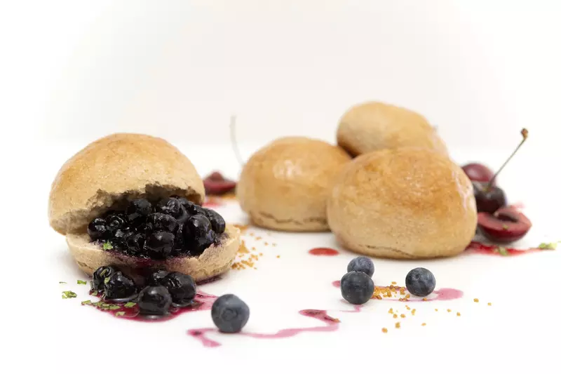 four fresh baked rolls, one covered in blueberries with a fruit syrup