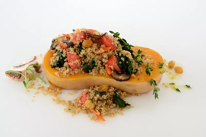 Quinoa, mixed with plum tomatoes, Swiss chard and mushrooms, placed in the center of a butternut squash half
