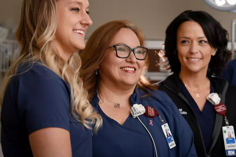 Three nurses stand together, smiling at something off the right side of the image.