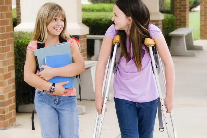 A girl on crutches walks with her friend at school