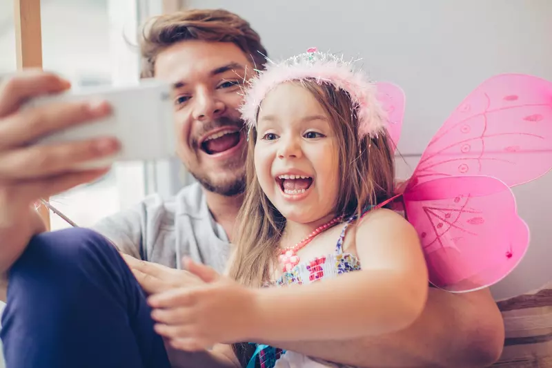 A dad and daughter take a selfie while playing dress up.