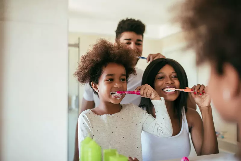 A young girl brushes her teeth with her parents as examples