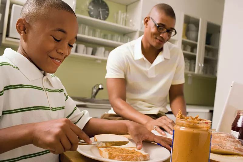 Father and son make peanut butter sandwiches together.
