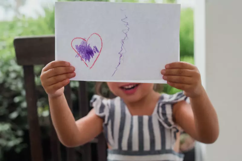 A little girl proudly displays her artwork for the camera.