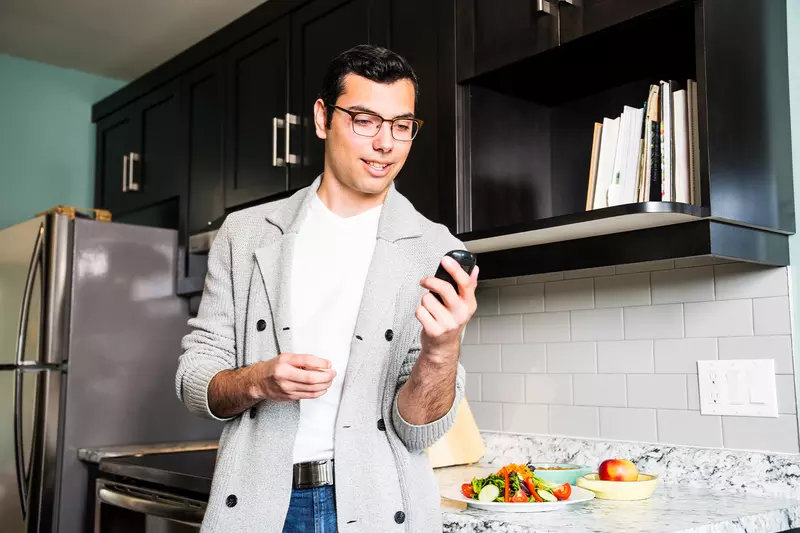 A Man Wearing Glasses Checks His Glucose Levels Before Eating a Healthy Meal in His Kitchen