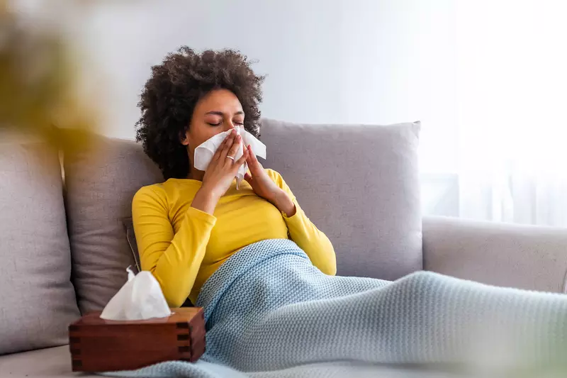 A woman sneezes on her couch at home